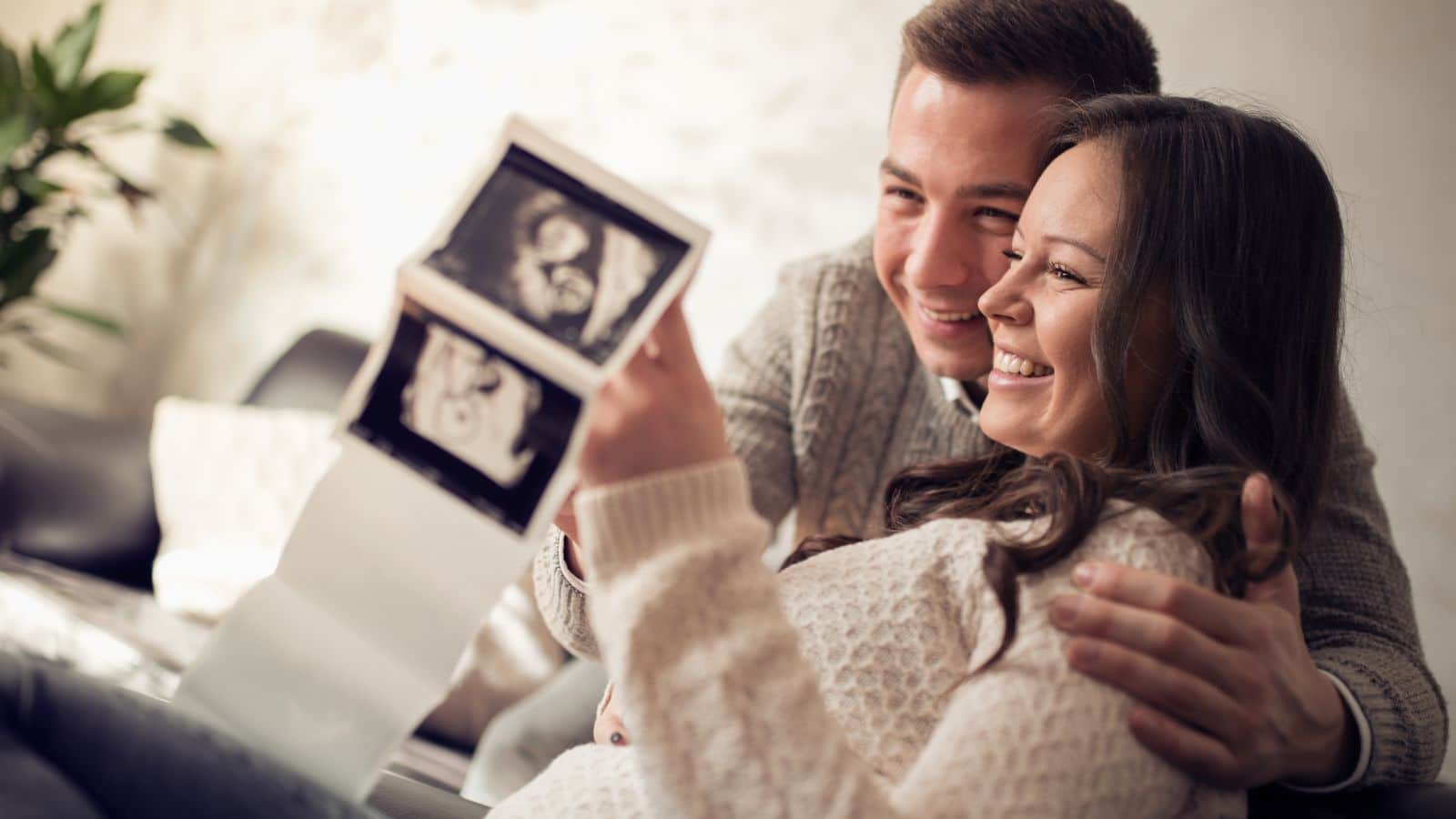 A married couple looking at sonogram pictures and smiling.