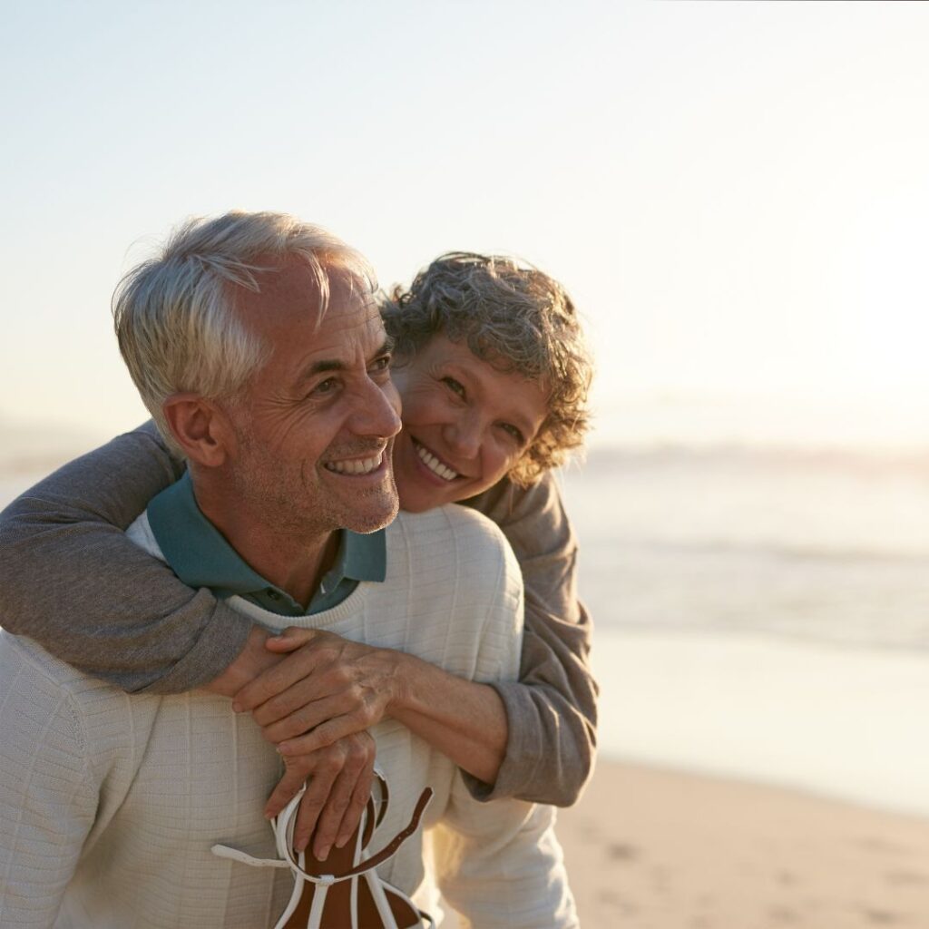 An older couple hugging by the beach.