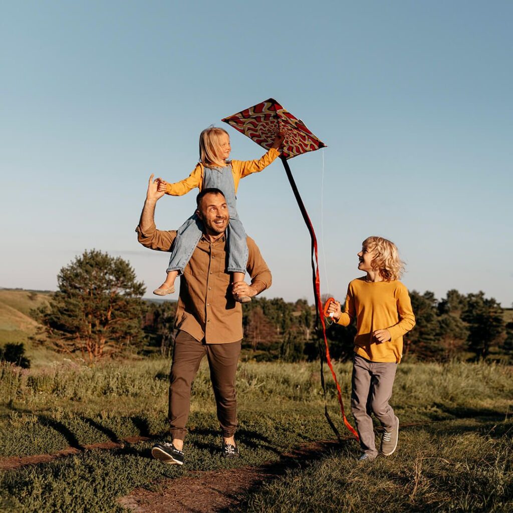 A father playing with his daughters in a field as they launch a kite.